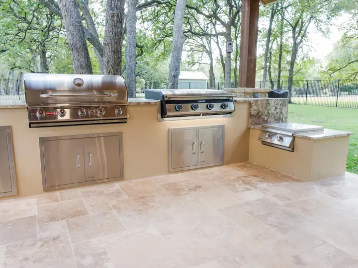 Outdoor kitchen with built-in grill, griddle, and stone counters under a cedar pavilion