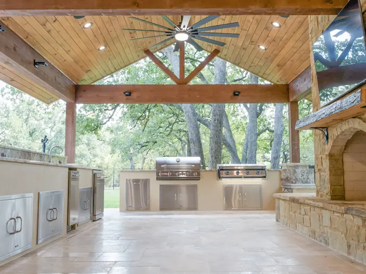 Vaulted cedar outdoor kitchen pavilion with ceiling fans and travertine floor