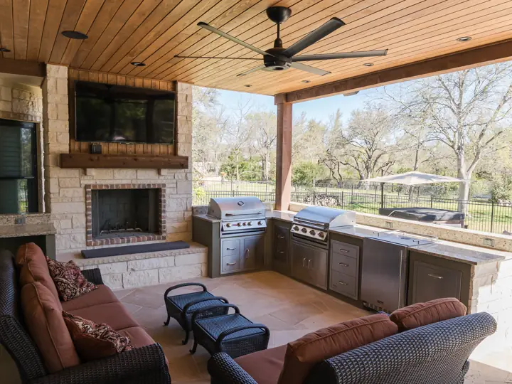 Covered outdoor living room with stone fireplace, outdoor kitchen, and cedar ceiling