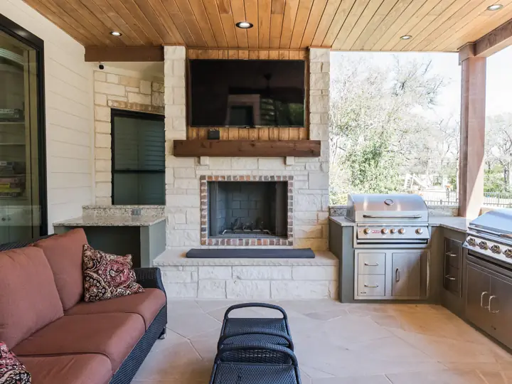 Outdoor stone fireplace with built-in wood storage and mounted TV