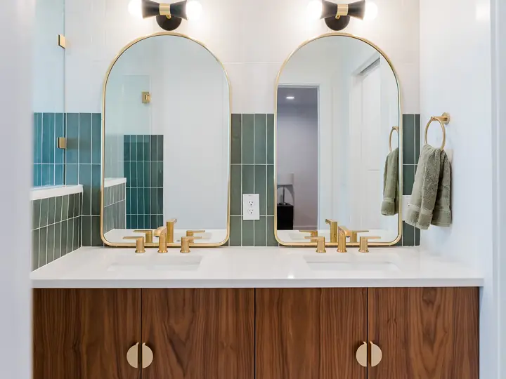 Bathroom vanity with walnut cabinets, arched mirrors, and green tile