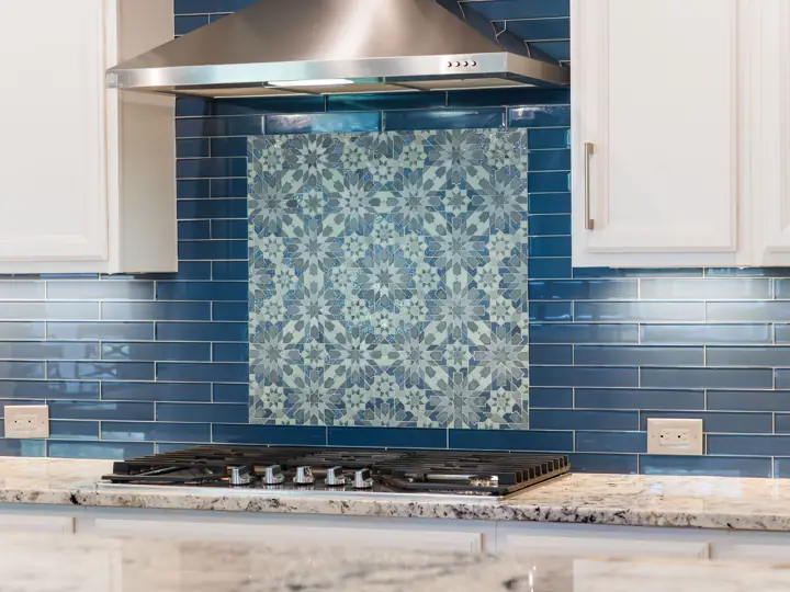 Blue glass tile backsplash with patterned mosaic focal point behind the range